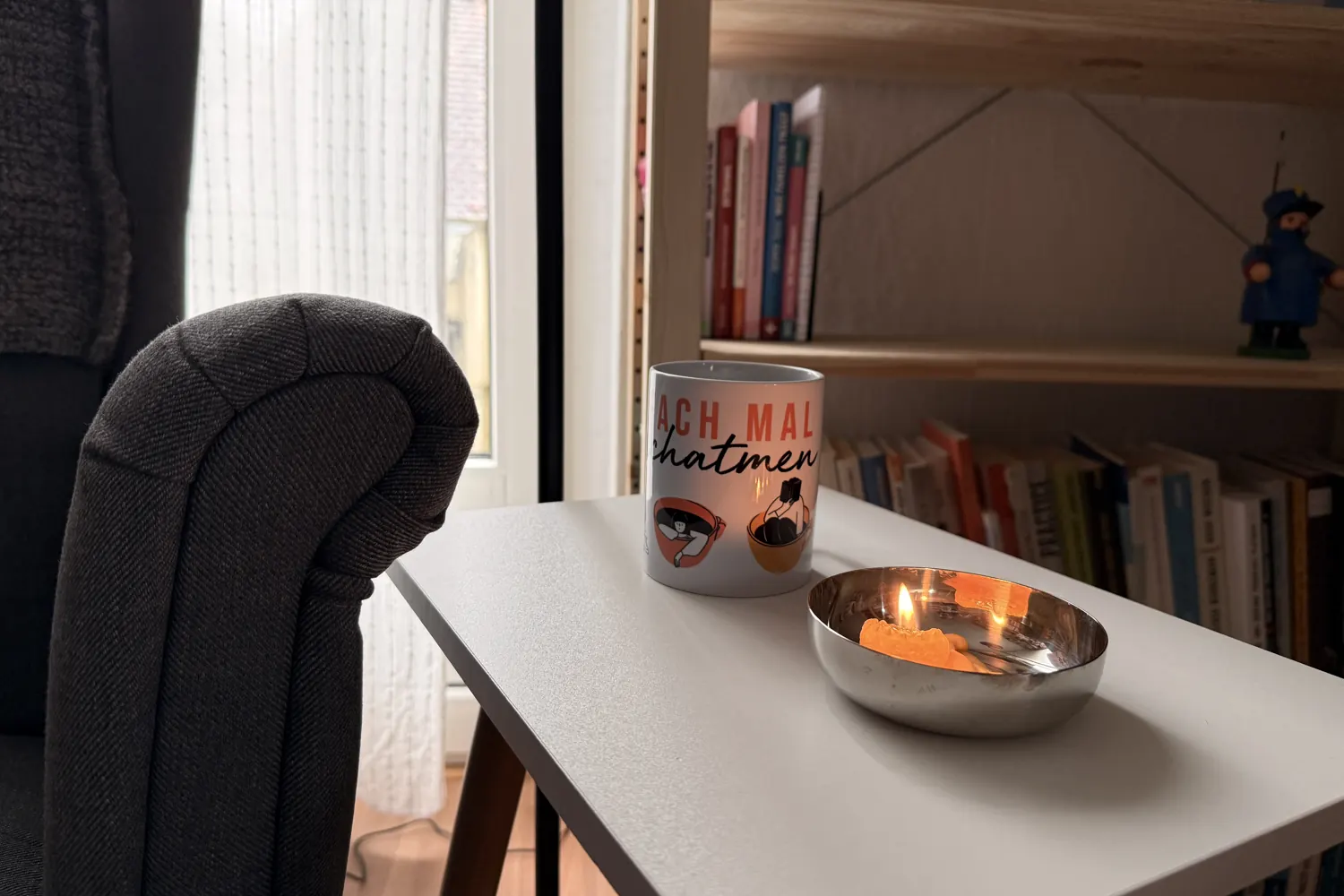 Sessel, kleiner Tisch und eine Schale mit Teelicht vor dem Bücherregal - Heiko Metz