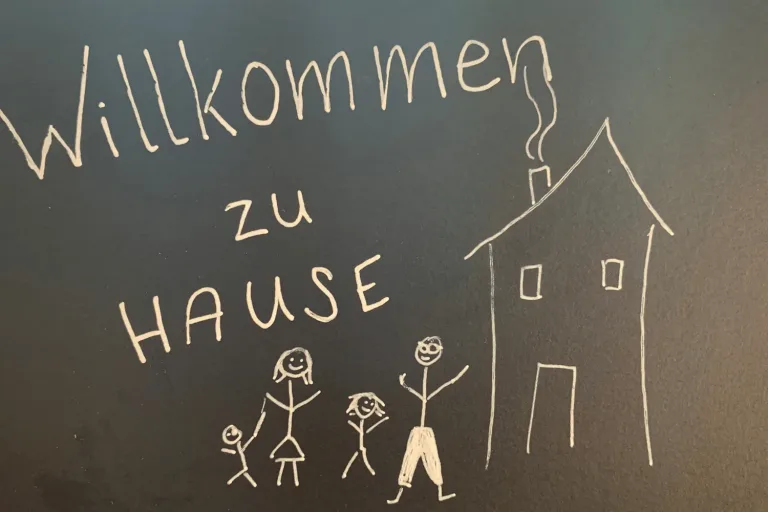Kreidetafel mit „Willkommen zu Hause“ und einer gemalten Familie vor einem Haus - Heiko Metz