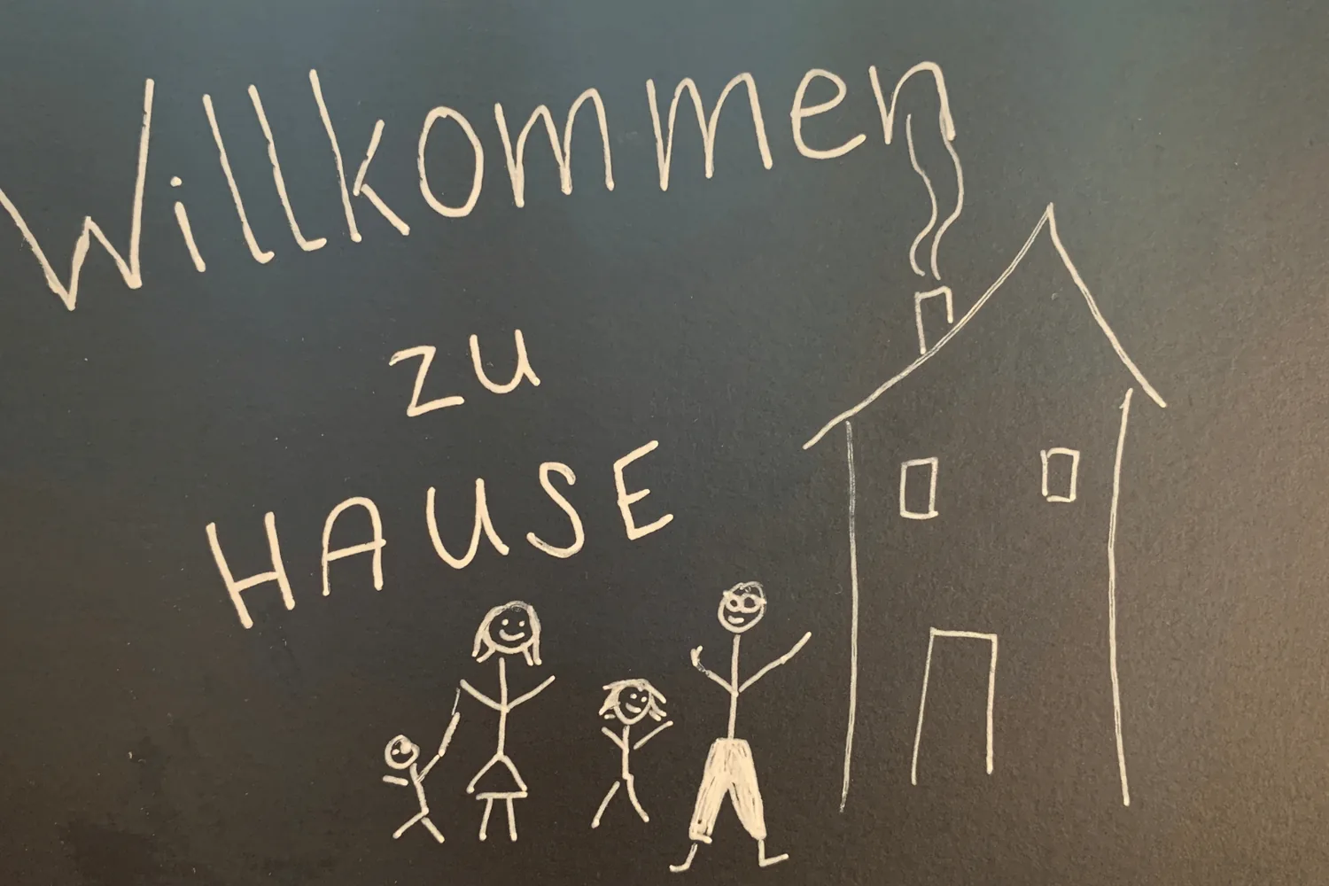 Kreidetafel mit „Willkommen zu Hause“ und einer gemalten Familie vor einem Haus - Heiko Metz