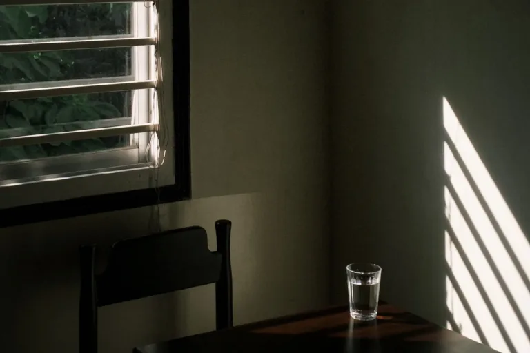 Fensterlicht in einem kargen Raum, ein Glas Wasser auf dem Tisch