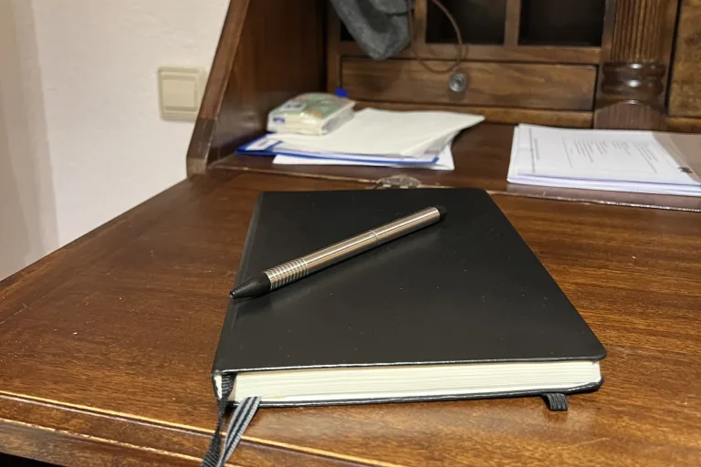 Schwarzes Notizbuch mit Stift auf einem alten Sekretär - Heiko Metz