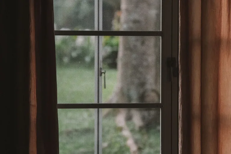 Offenes Fenster mit Vorhängen, draußen ein Garten