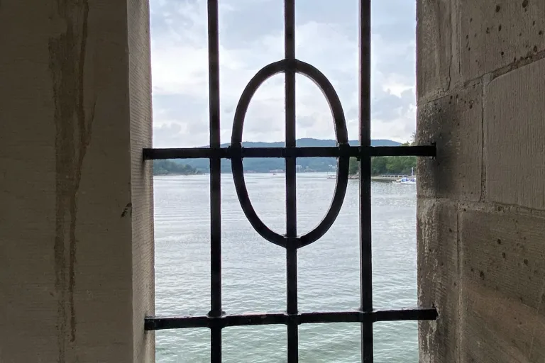 Fenster mit Eisengitter, dahinter Wasser und Hügel - Heiko Metz
