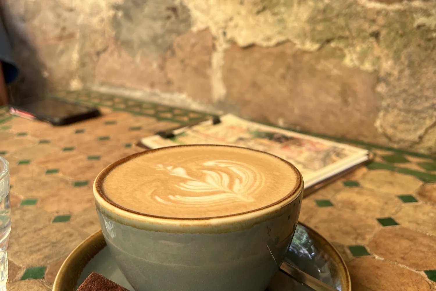 Cappuccino auf einem Mosaiktisch vor einer Sandsteinwand - Heiko Metz