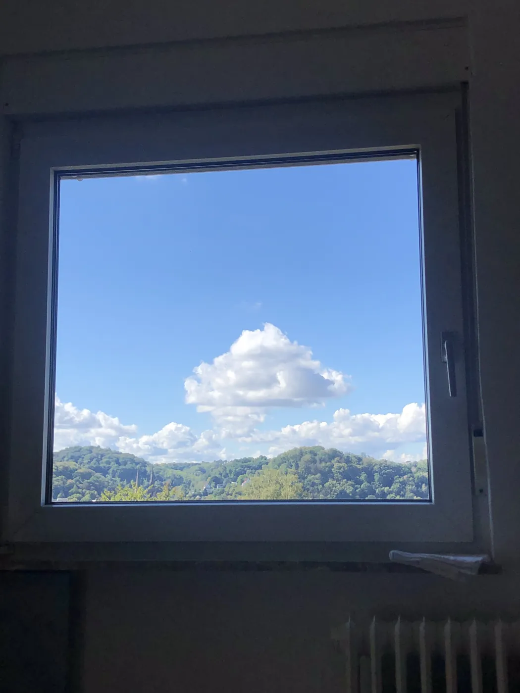 Fenster in einer dunklen Wand, dahinter blauer Himmel mit Wolken über bewaldeten Hügeln - Heiko Metz